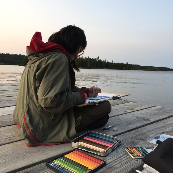 teenager sitting on a dock with a tray of colored pencils