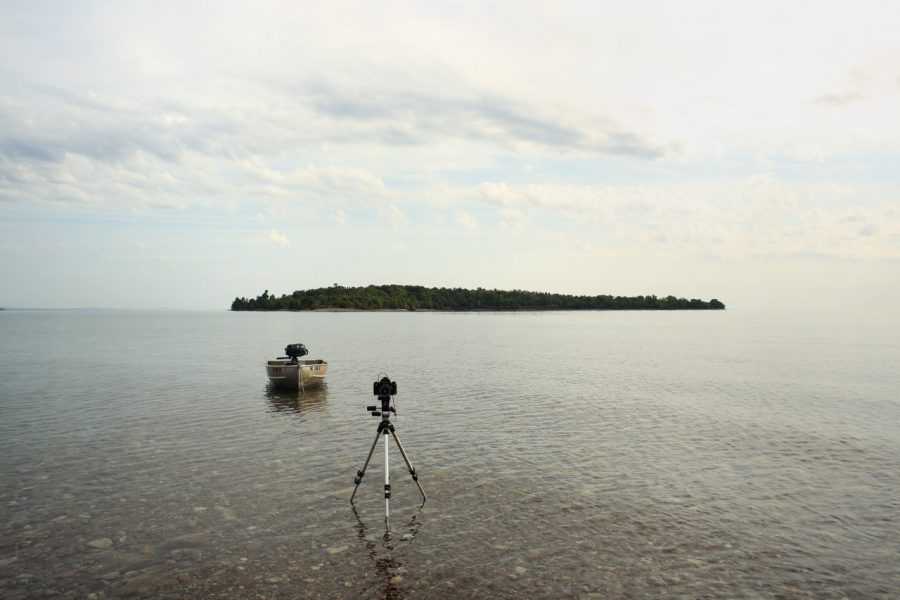 Island in grey water with a camera on a tripod and small fishing boat